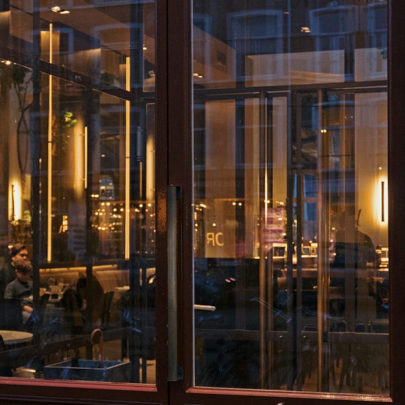 Glass restaurant doors at dusk, the dining room glowing behind them: the new front door of hospitality