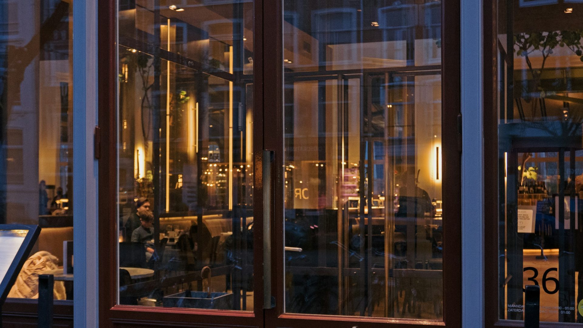 Glass restaurant doors at dusk, the dining room glowing behind them: the new front door of hospitality
