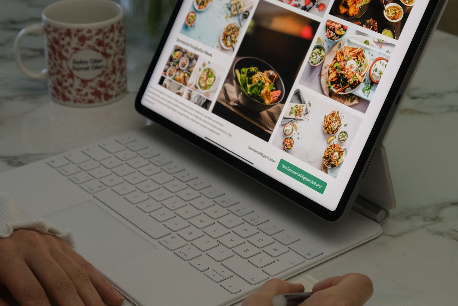Hands using a tablet and keyboard for digital planning in a kitchen setting