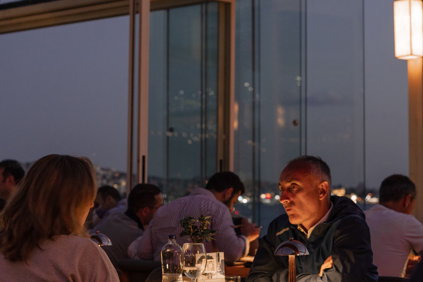Guests dining at a rooftop restaurant overlooking the city in the evening