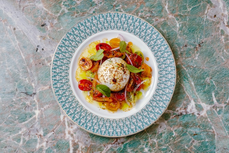 Seasonal tomato and burrata salad plated on a marble surface.