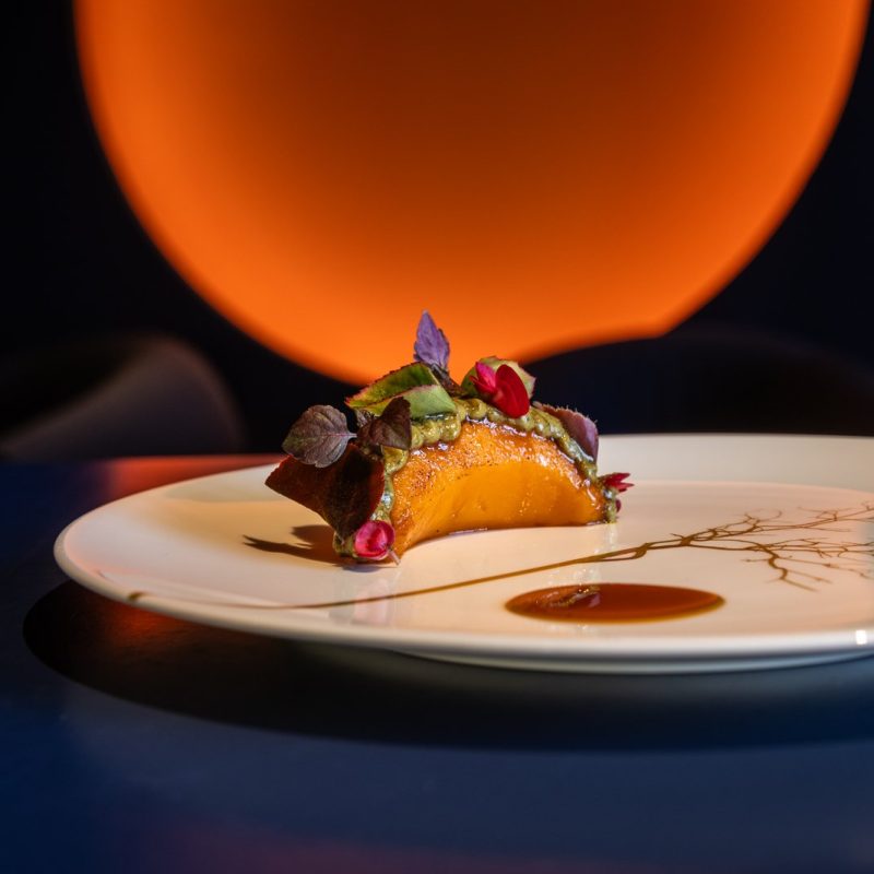 A plated dish at Agli Amici against a warm orange background.