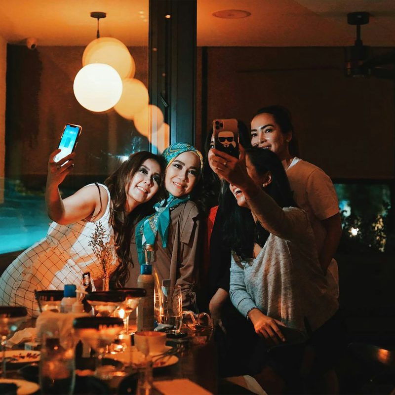 Friends taking selfies at a candlelit restaurant dinner table