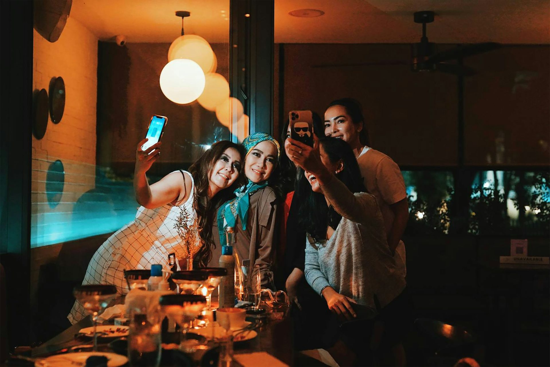 Friends taking selfies at a candlelit restaurant dinner table