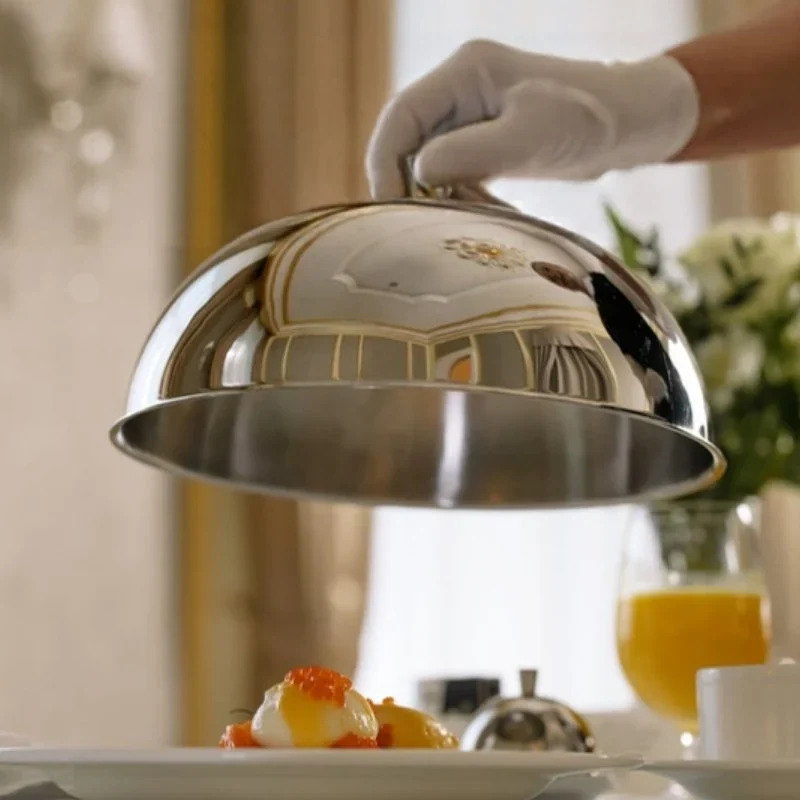 A white-gloved waiter lifts a silver cloche at a luxury hotel table